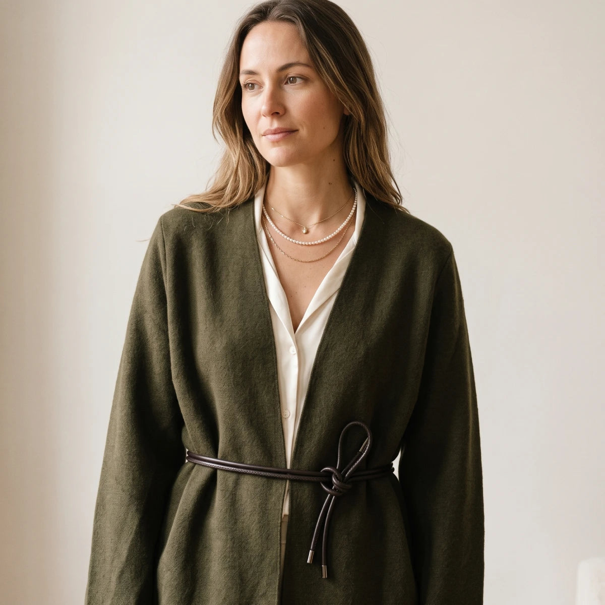 Mujer con cárdigan cruzado verde oliva con cnturón anudado, camisa blanca y collares dorados y de perlas Kloreys