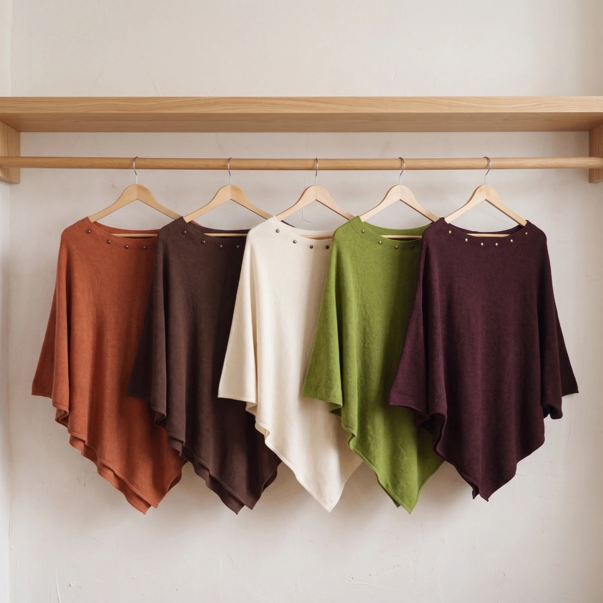 Cinco ponchos de colores con tachuelas en el escote colgados en una barra de madera sobre
pared blanca