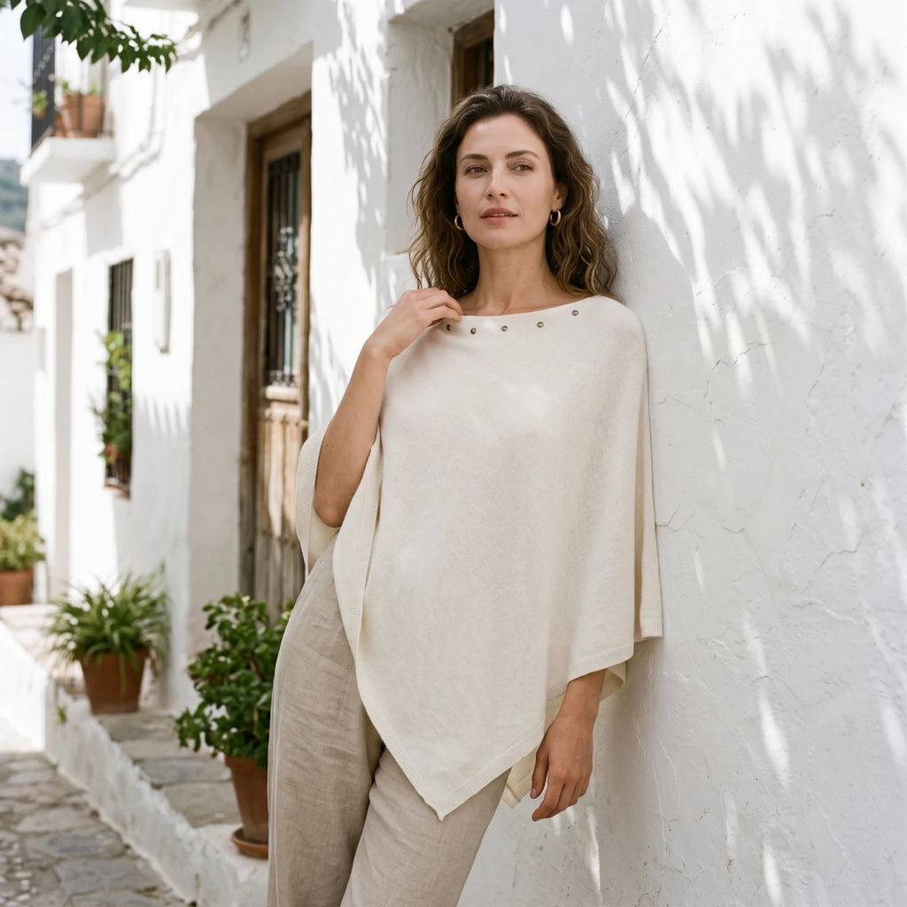 mujer apoyada en la pared con el poncho blanco con tachuelas y pantalón de lino beige Kloreys