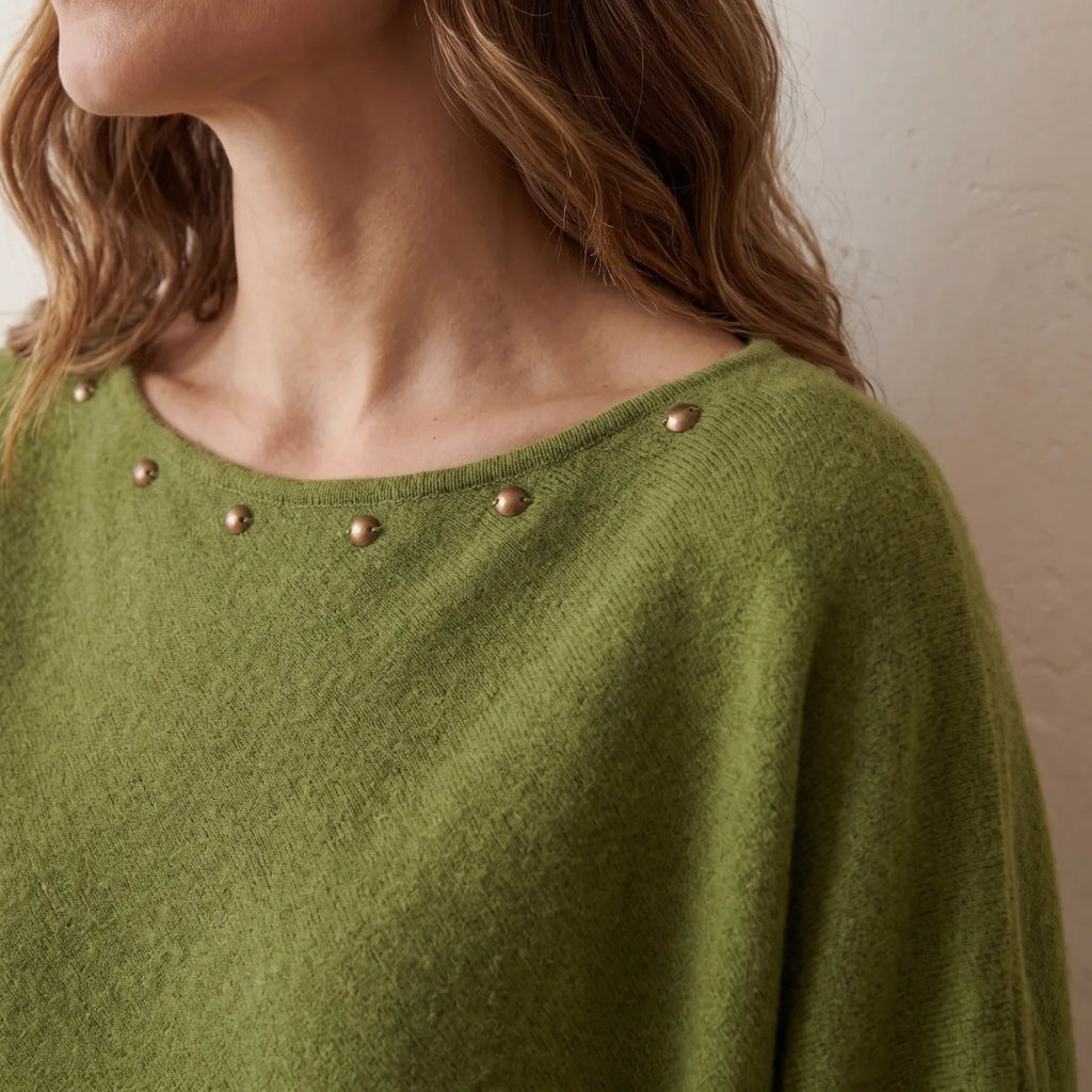 Primer plano del escote ancho del poncho verde con tachuelas metálicas cosidas Kloreys