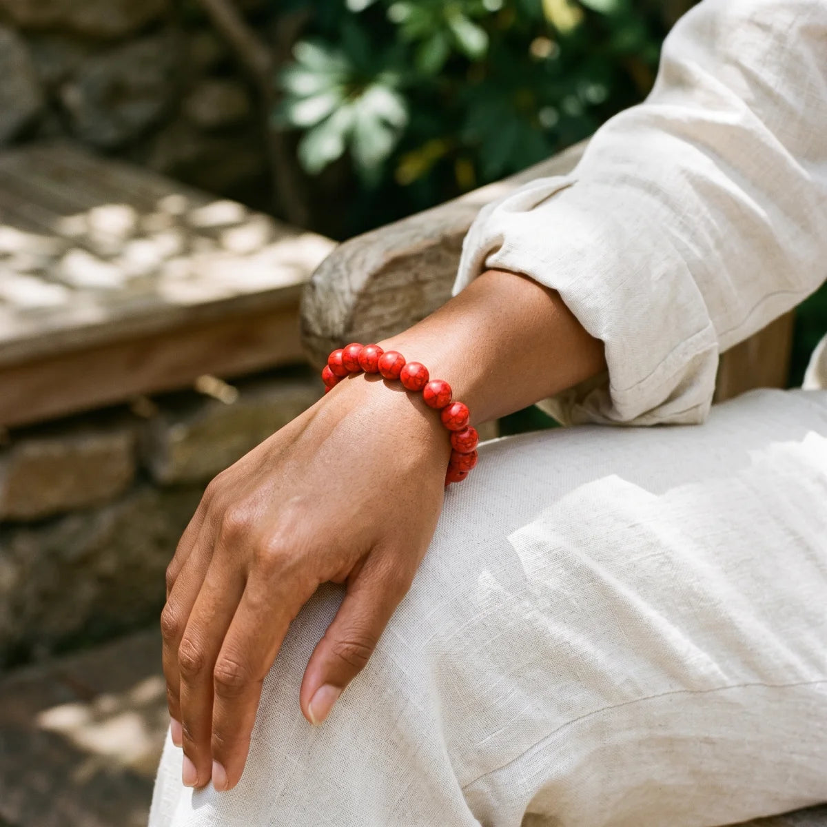 Pulsera elástica de howlita roja con bolitas de piedra en muñeca con pantalón de lino
