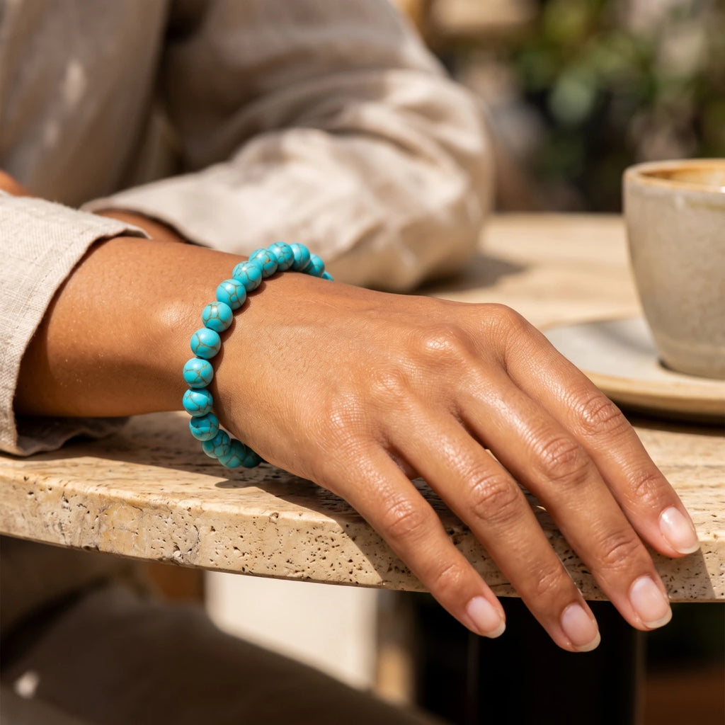 Pulsera elástica de howlita azul turquesa 8 mm en muñeca de mujer con ropa de lino
