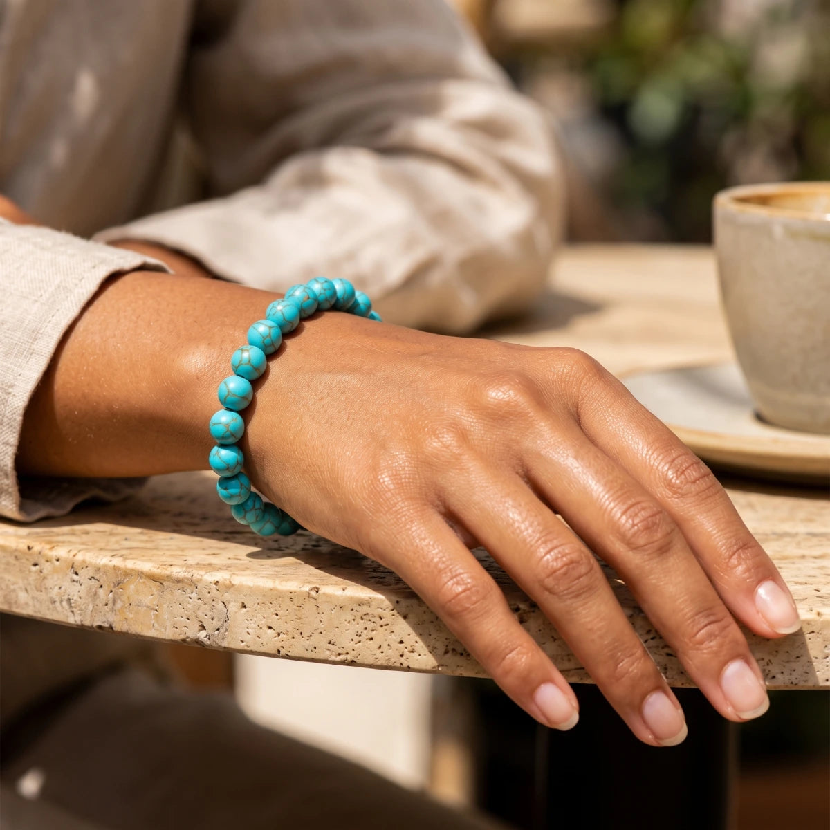 Pulsera elástica de howlita azul turquesa 8 mm en muñeca de mujer con ropa de lino