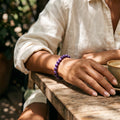 Pulsera de amatista elástica en la muñeca de una mujer sobre una mesa de madera en una terraza