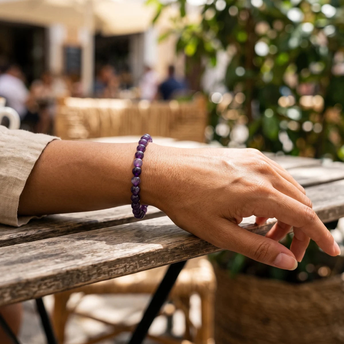 Pulsera de amatista elástica en la muñeca de una mujer sobre una mesa de madera en una terraza